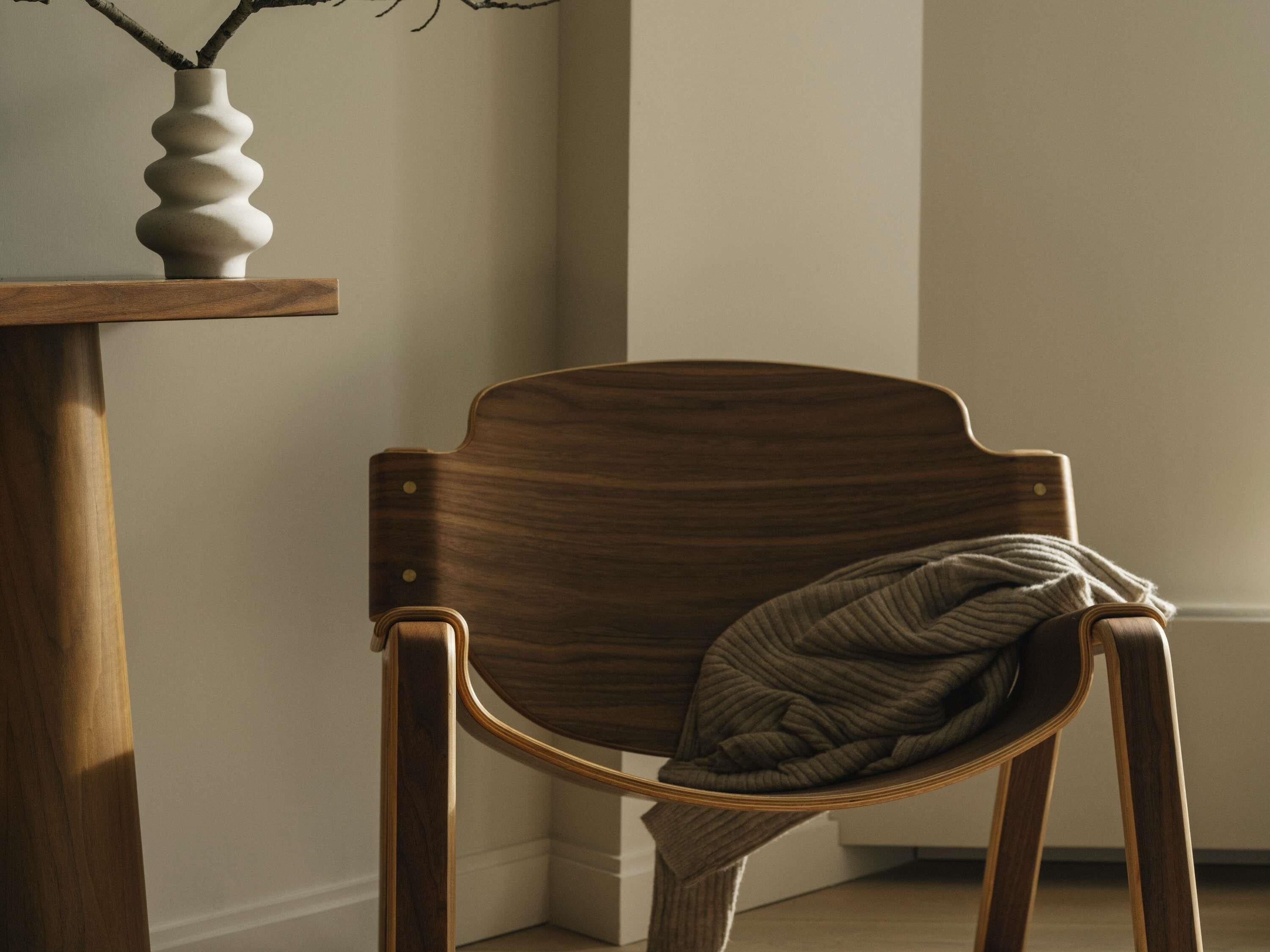 Ein Holzstuhl mit Kissen, ein Holztisch mit einer Vase und eine schlichte Wand.