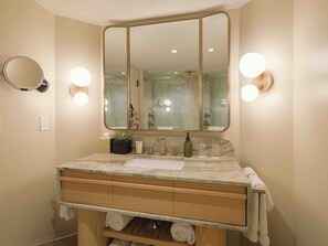 A bathroom with a large mirror, two wall-mounted lights, a sink, and a wooden vanity with drawers and a shelf.