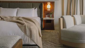 A hotel room with a large bed, a bedside table with a lamp, a chair, and a patterned carpet.