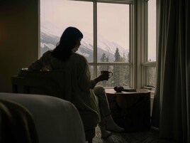 Una persona sentada junto a una ventana con vistas a montañas nevadas.