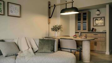 Ett modernt vardagsrum med en soffa, ett matbord och en köksdel med träskåp och en hängande lampa.