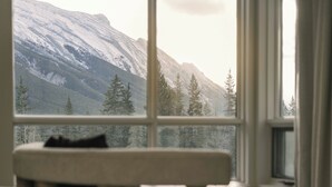 A room with a bed and a window overlooking a snowy mountain landscape. - Rimrock Banff, Emblems Collection (Banff)