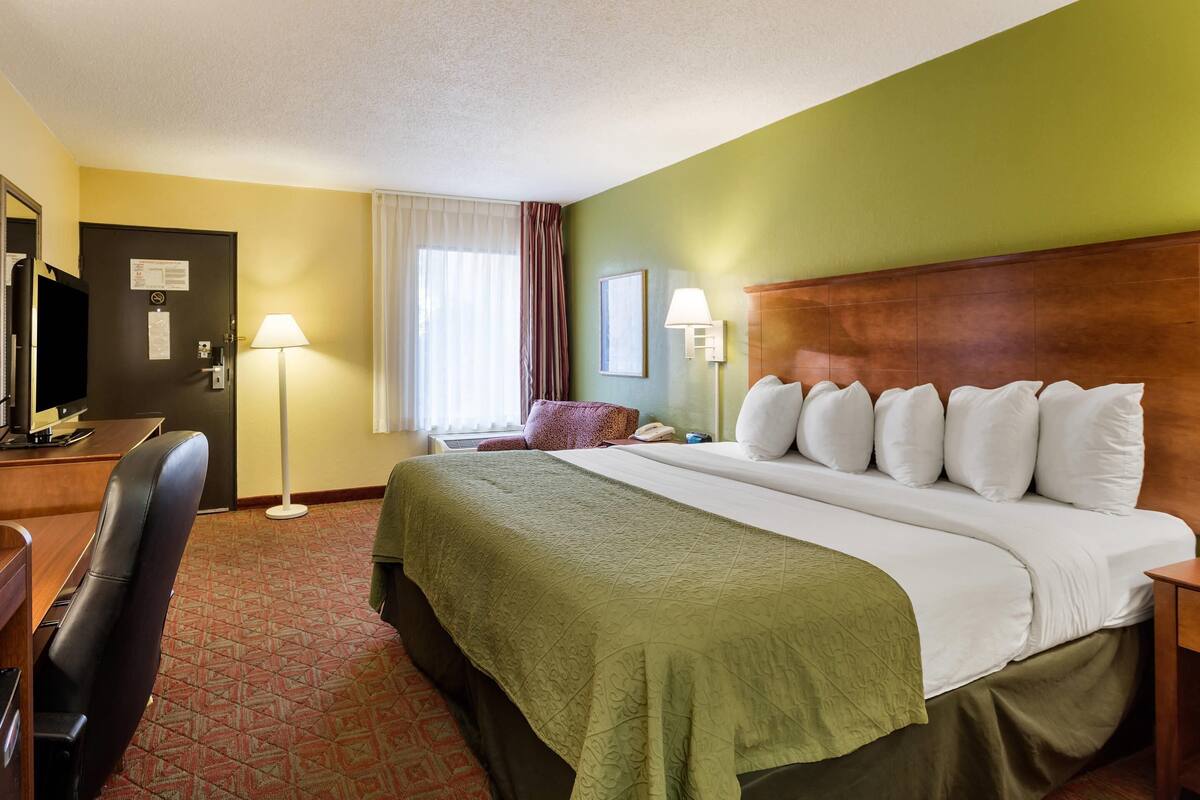 Une chambre d’hôtel équipée d’un lit, d’un bureau, d’une chaise, d’une lampe et offrant une vue sur l’extérieur.
