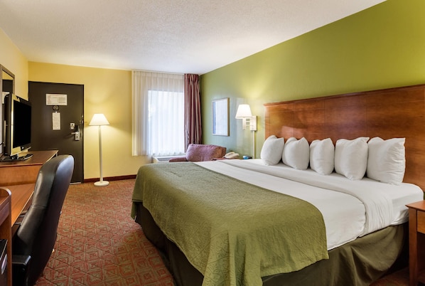 Habitación de hotel con cama, escritorio, silla, lámpara y vistas al exterior.