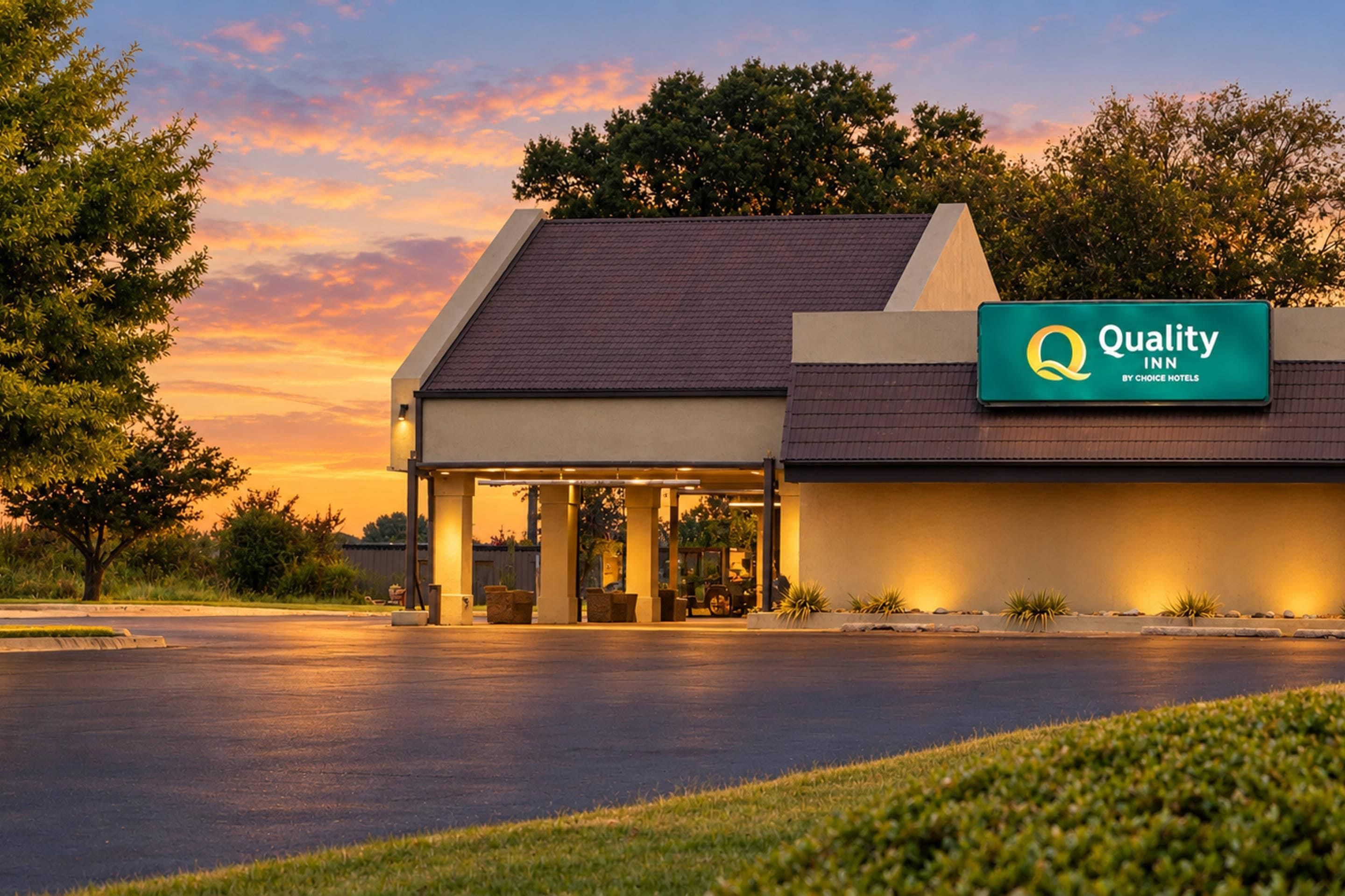 A hotel with a covered entrance, a sign indicating it is a Quality Inn by Choice Hotels, and a parking lot in front.