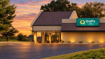 A hotel with a covered entrance, a sign indicating it is a Quality Inn by Choice Hotels, and a parking lot in front.