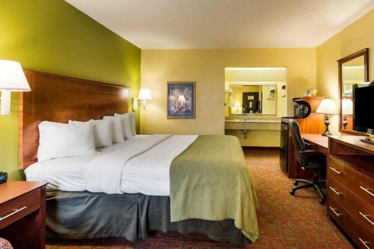 Une chambre d’hôtel équipée d’un lit, d’un bureau, d’une chaise, d’une commode, d’un miroir et d’un téléviseur.