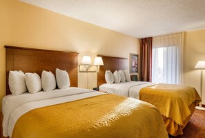 Une chambre d’hôtel avec deux lits, chacun doté d’une tête de lit, de draps blancs et d’une couvre-lit jaune. On y trouve deux lampes de chevet, une fenêtre avec des rideaux et un tableau encadré au mur.