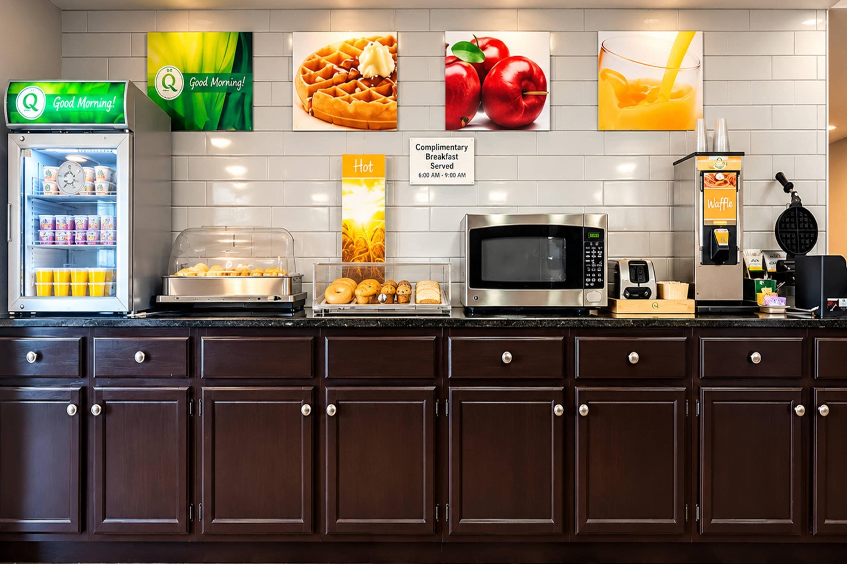 A breakfast area with a refrigerator, microwave, waffle maker, and various food items.