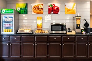 A breakfast area with a refrigerator, microwave, waffle maker, and various food items. - Quality Inn Blytheville (Blytheville)