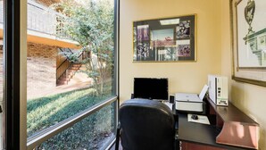Een kamer met een bureau, computer en een raam met uitzicht op een binnenplaats.