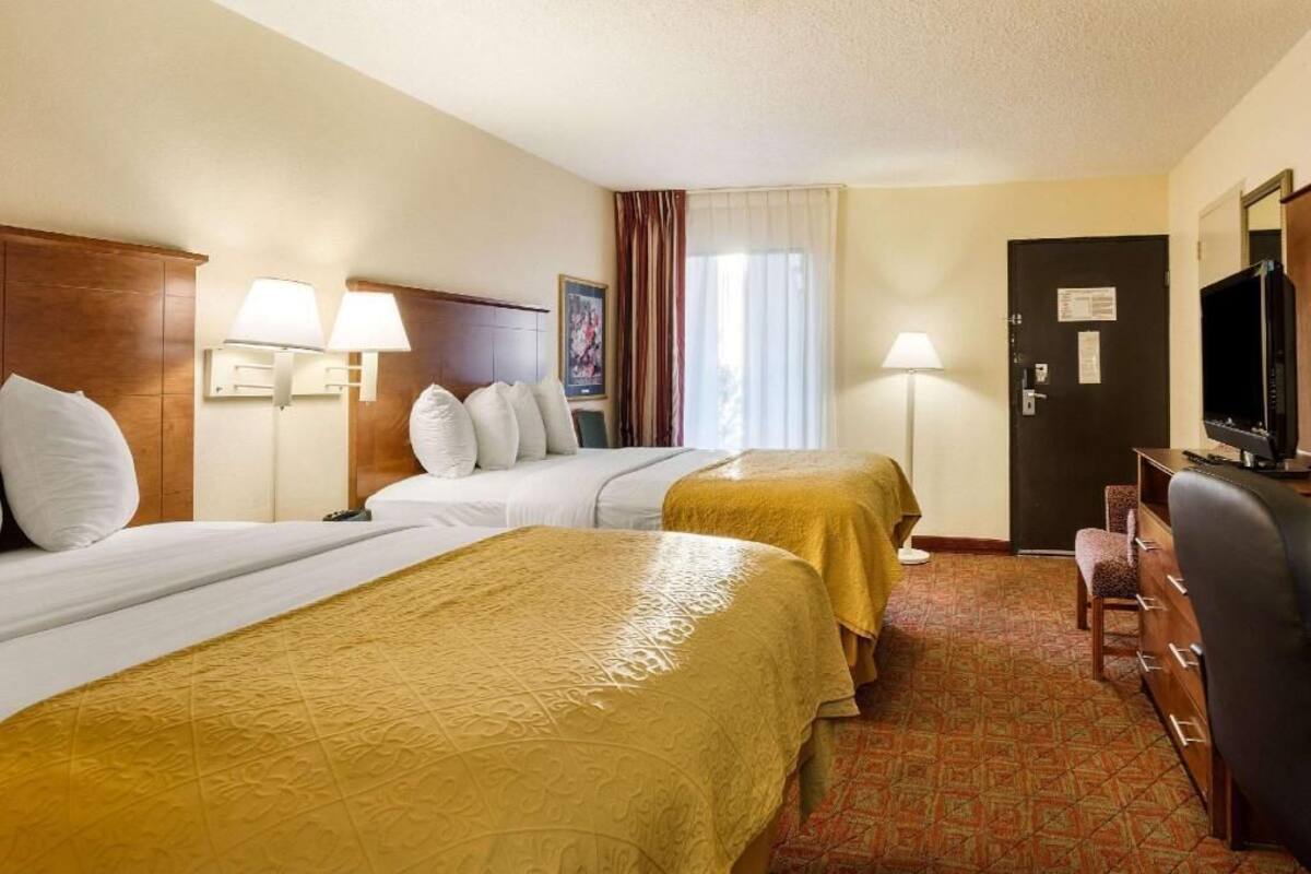 Une chambre d’hôtel avec deux lits, un bureau, une télévision et une porte sur laquelle est affiché un avis.