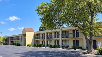 A motel with a parking lot and a tree in the foreground.