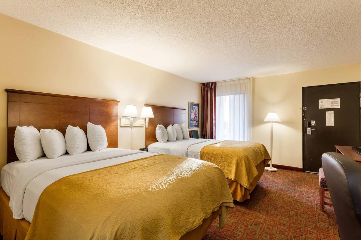 Une chambre d’hôtel avec deux lits, un bureau, une chaise, une lampe et une porte sur laquelle est affiché un avis.