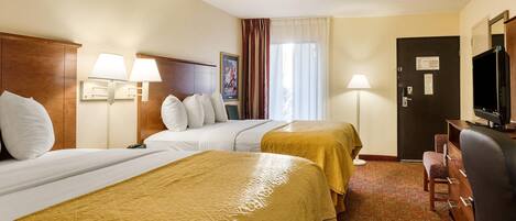 A hotel room with two beds, a desk, a chair, a television, and a door with a sign.