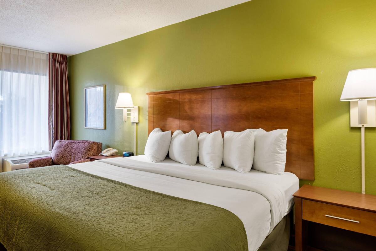 Une chambre d’hôtel avec un lit, des lampes de chevet, une table de chevet, une chaise et une fenêtre avec des rideaux.