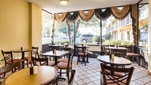 Een restaurant met meerdere tafels en stoelen, grote ramen met gordijnen en een uitzicht op de straat.