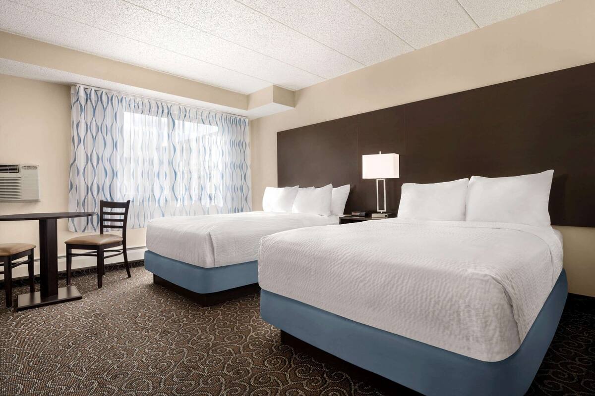A hotel room with two beds, a desk, a chair, a lamp, and a patterned carpet.