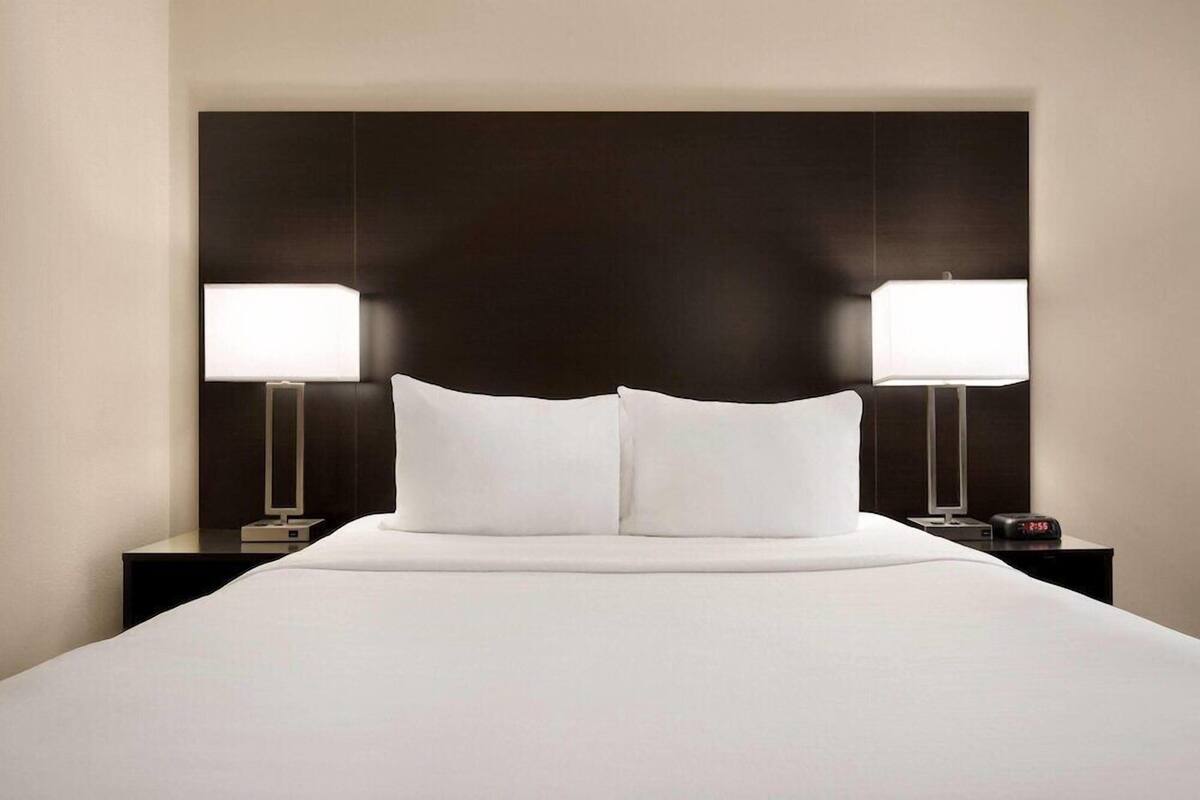 A hotel room with a large bed, two bedside tables with lamps, and a dark headboard.