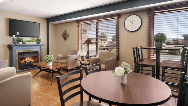 A hotel room with a fireplace, comfortable seating, a round dining table, and large windows with blinds. - Days Inn by Wyndham Fort Collins (Fort Collins)