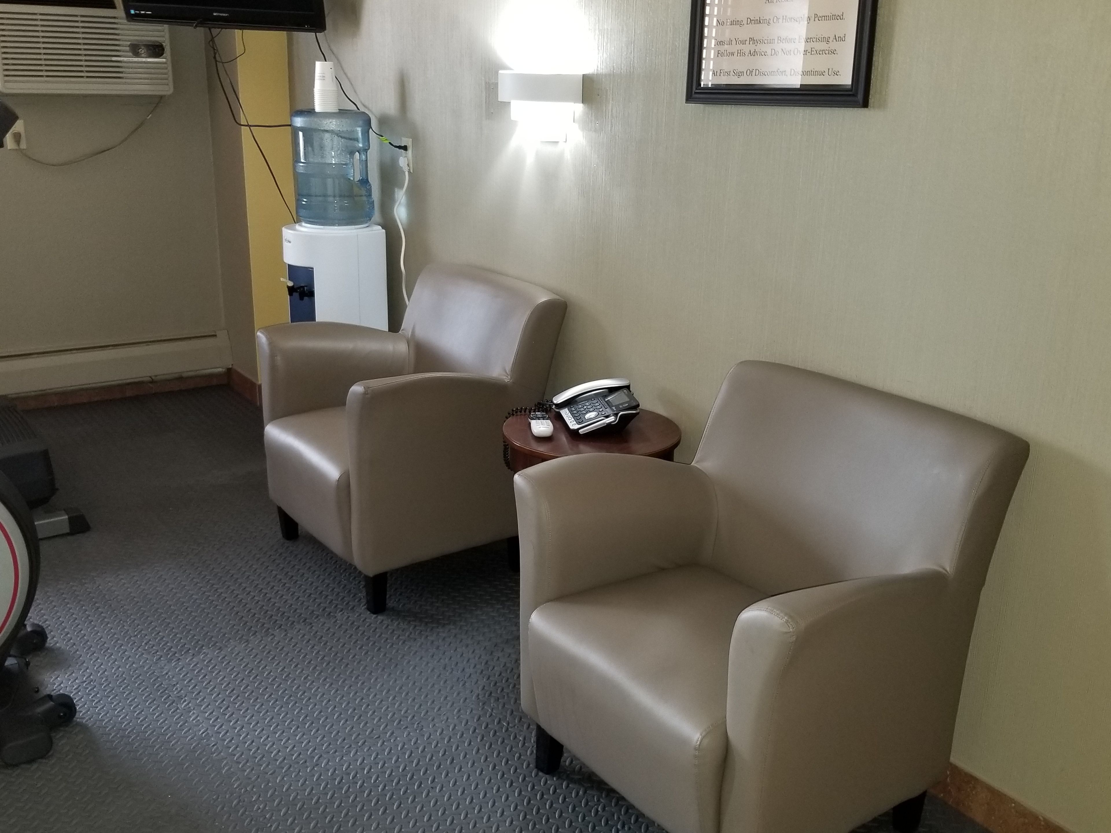 Una habitación con dos sillones color beige, una mesita con un teléfono, un dispensador de agua y una lámpara de pared.