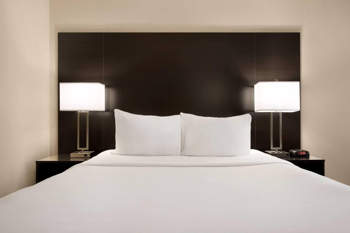 A hotel room with a large bed, two bedside tables with lamps, and a dark headboard.
