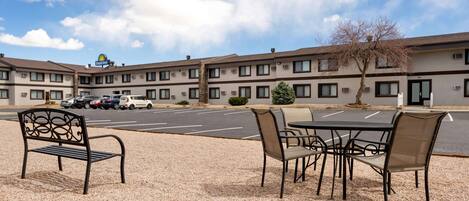 A motel with a parking lot, outdoor seating area, and a clear sky.