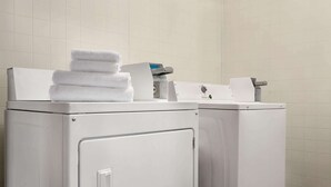 A laundry area with stacked white towels on a dryer and a washing machine. - Days Inn by Wyndham Fort Collins (Fort Collins)