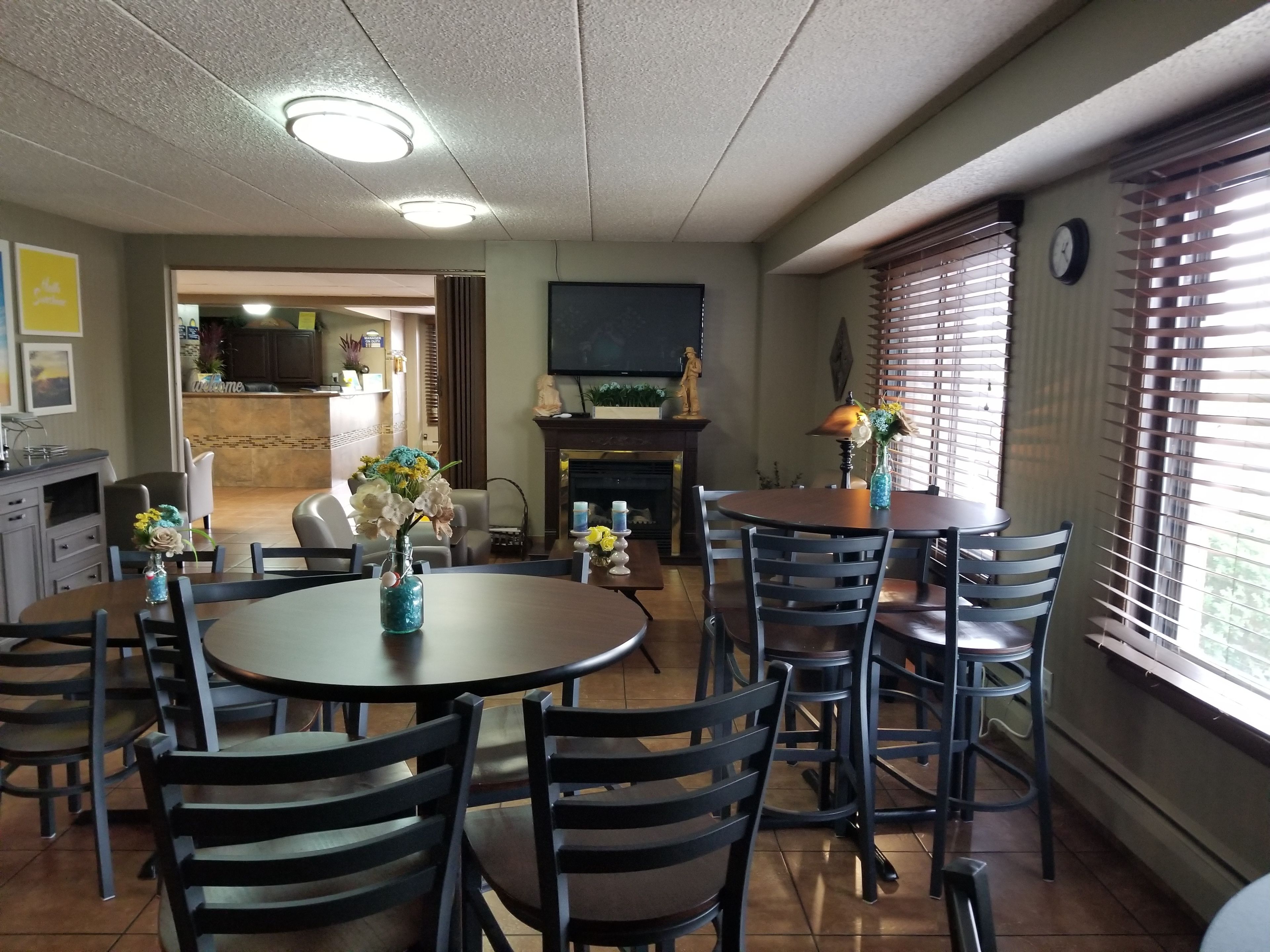 Un espace repas avec des tables et des chaises rondes, une cheminée et un téléviseur fixé au mur.