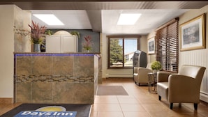 A reception area with a reception desk, a clock, a plant, a chair, and a door. - Days Inn by Wyndham Fort Collins (Fort Collins)