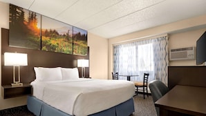 A hotel room with a large bed, two bedside tables with lamps, a desk with chairs, and a large window with curtains. - Days Inn by Wyndham Fort Collins (Fort Collins)
