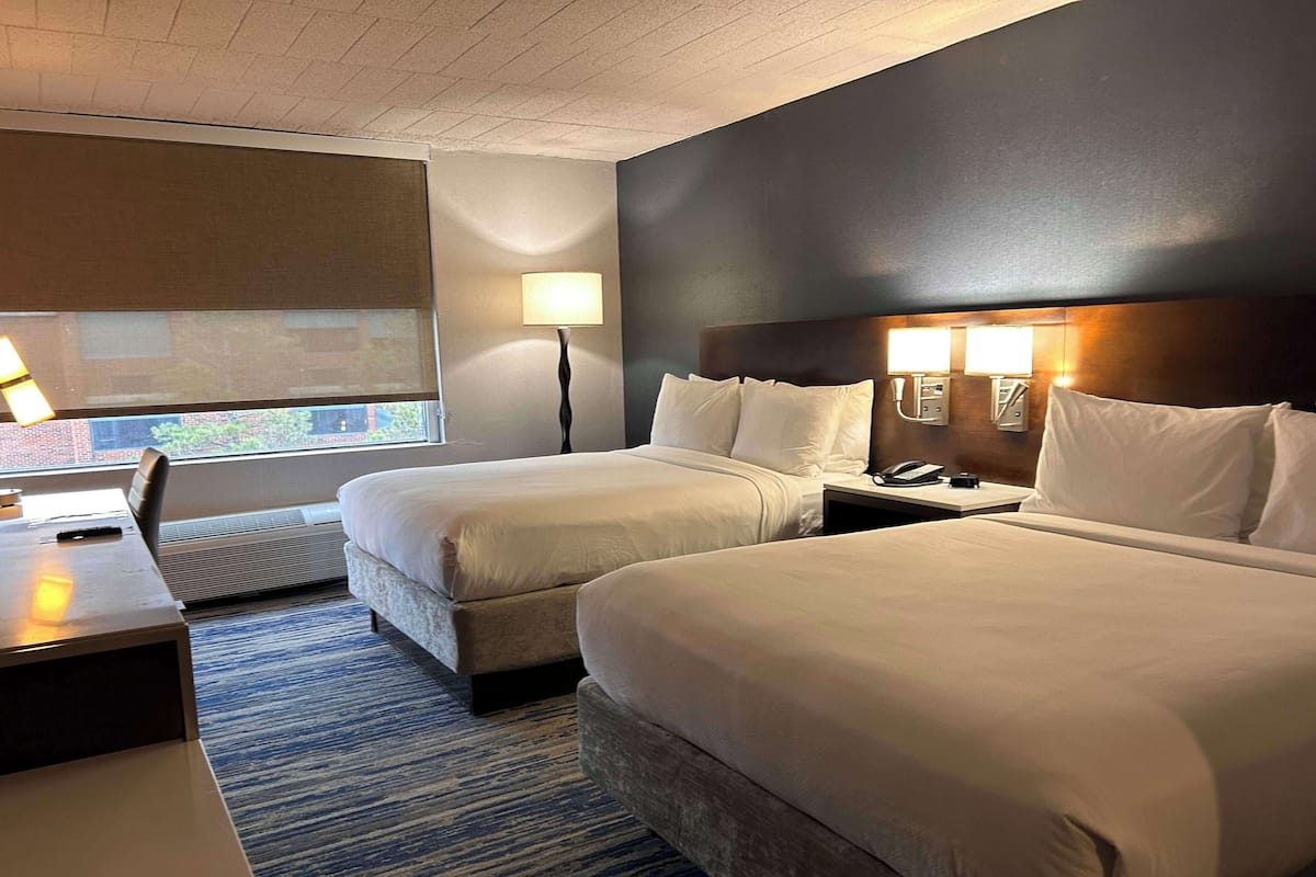 A hotel room with two beds, a desk, a lamp, and a phone on the nightstand.