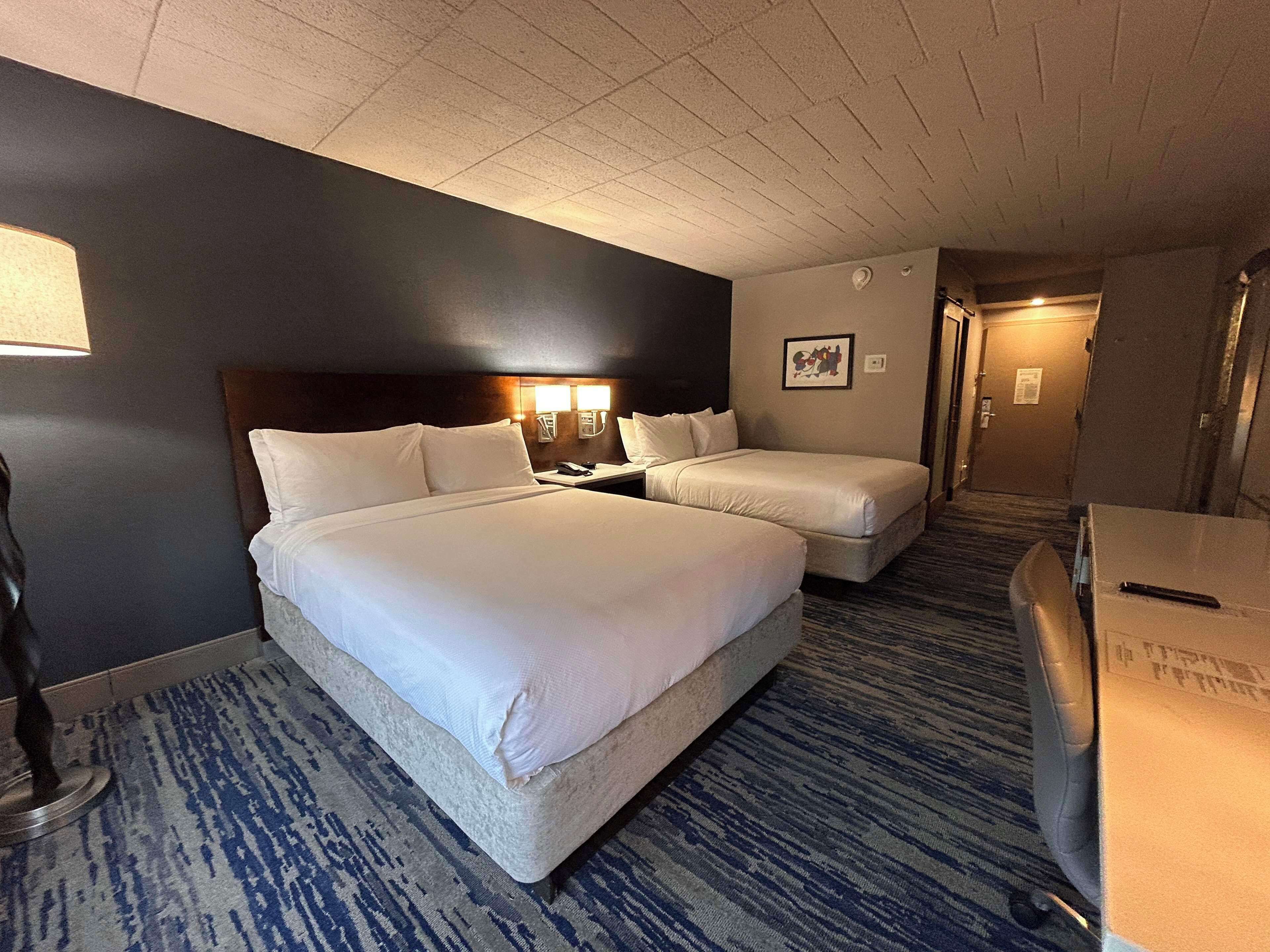 A hotel room with two beds, a desk, a lamp, and a carpeted floor.