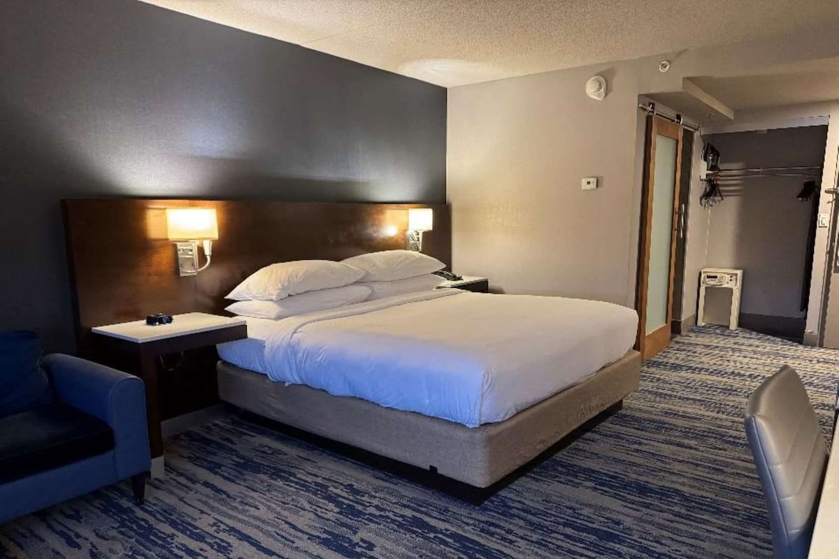 A hotel room with a bed, bedside tables, a chair, and a carpeted floor.