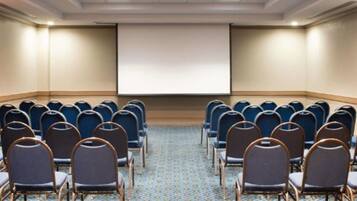 Un salón de conferencias con filas de sillas mirando hacia una pantalla de proyección.