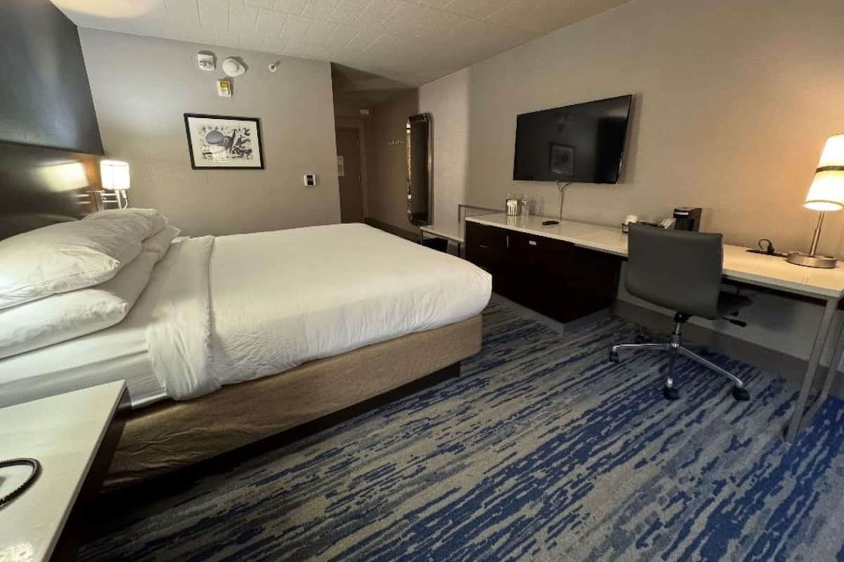 A hotel room with a bed, desk, chair, TV, and a bathroom visible through an open door.