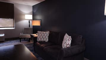 A dark-themed room with a sofa, patterned armchair, and a table.
