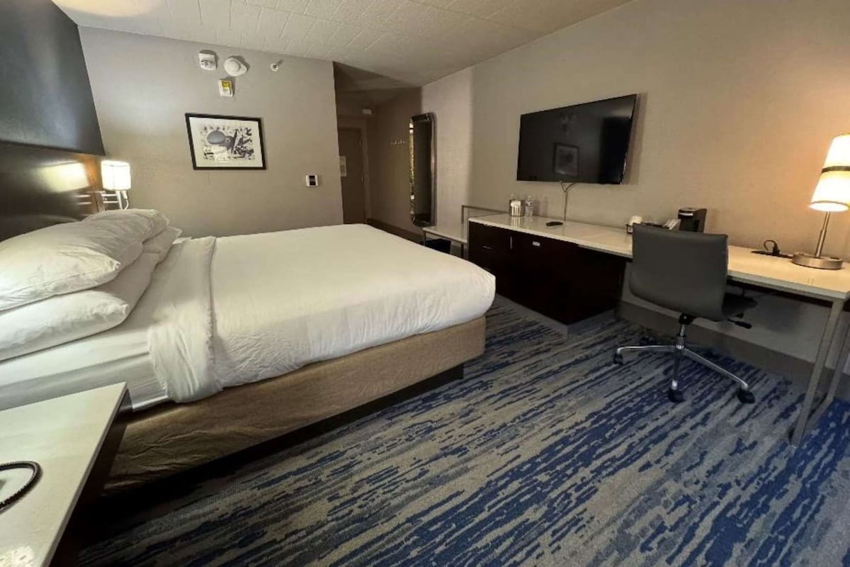 A hotel room with a bed, desk, chair, TV, and a bathroom.