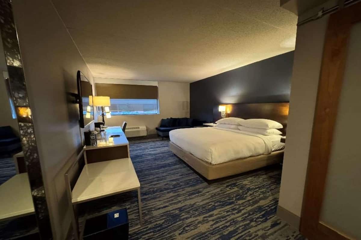 A hotel room with a bed, a desk with a chair, a TV, and a window.