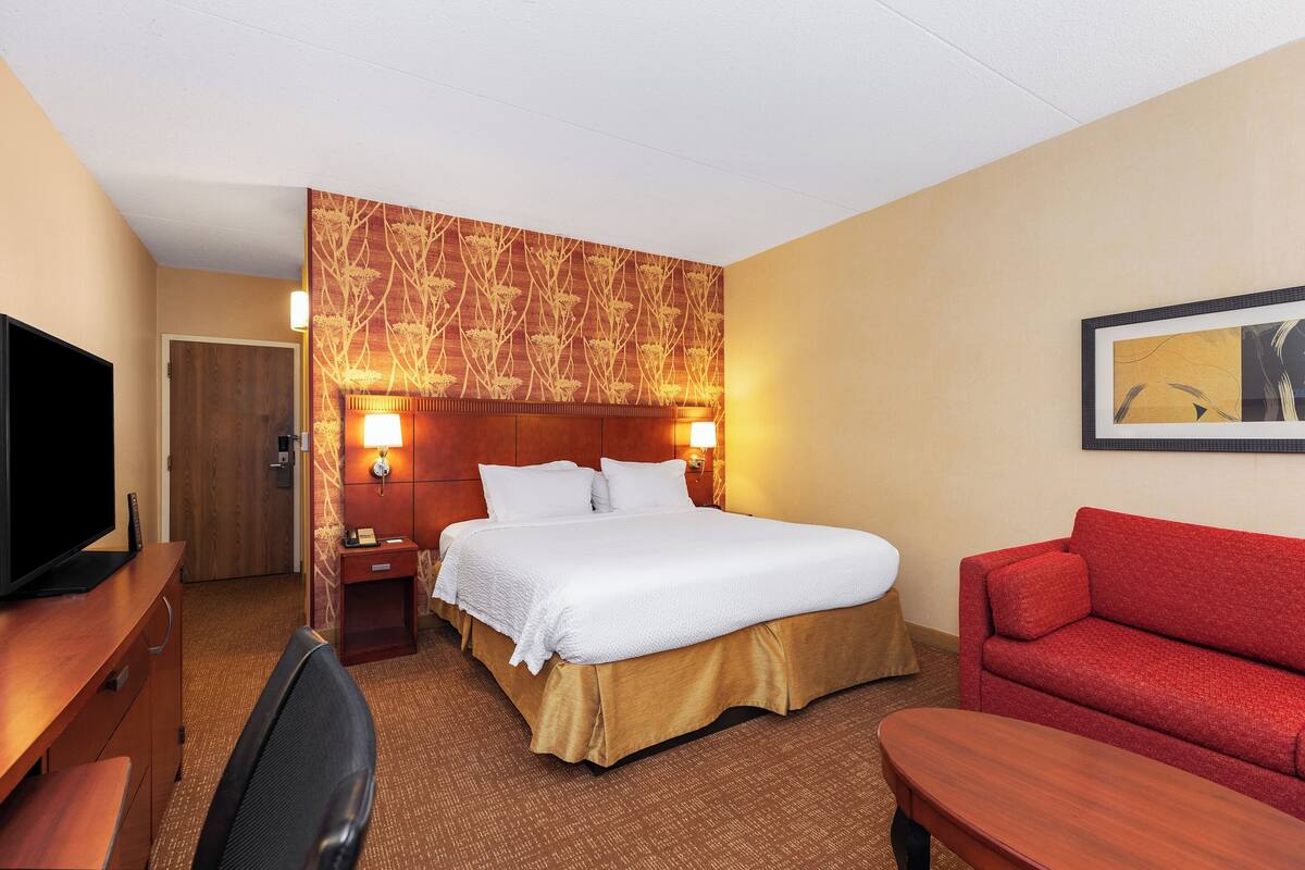 Una habitación de hotel con una cama, un televisor, un sofá rojo y un escritorio.