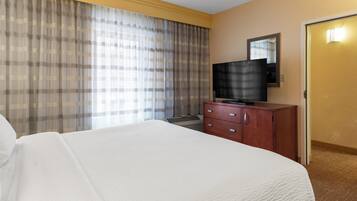 A hotel room with a large bed, a television on a wooden dresser, and a window with curtains.