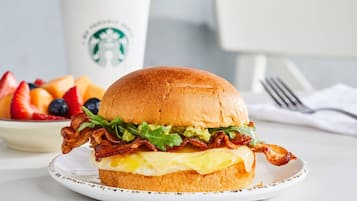 A breakfast sandwich on a plate with a Starbucks cup in the background.