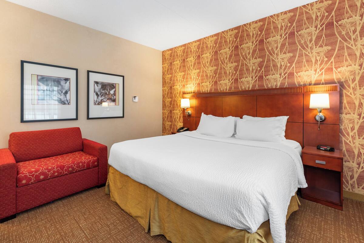 Habitación de hotel con una cama grande, un sofá rojo, dos cuadros en la pared y un papel tapiz estampado.