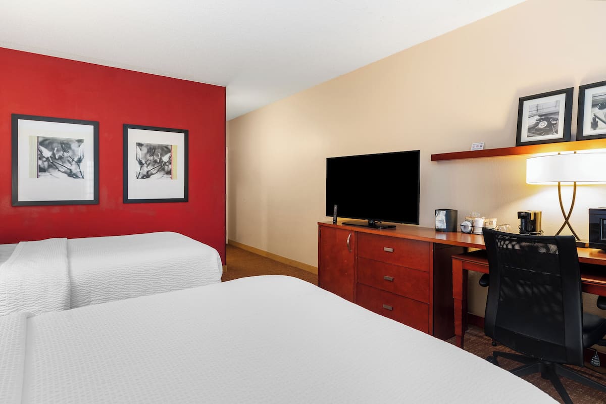 Habitación de hotel con dos camas, un escritorio con computadora, televisión y cuadros en la pared.