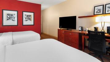 A hotel room with two beds, a desk with a computer, a television, and framed pictures on the wall.
