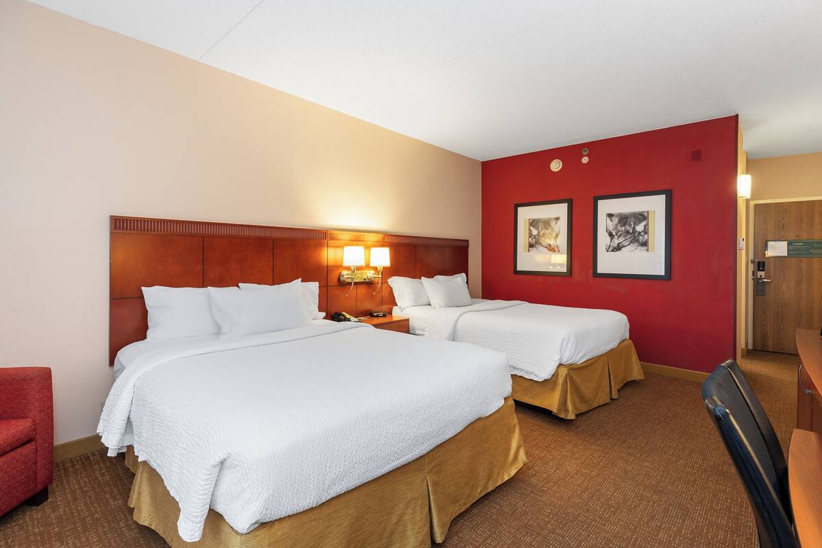 Habitación de hotel con dos camas, una pared decorada en rojo y un cabecero de madera.