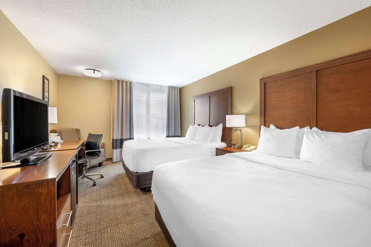 A hotel room with two beds, a desk with a television, a lamp, and a nightstand with a phone.