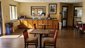 Une cuisine d’hôtel avec des placards en bois, un four à micro-ondes et un évier. On y trouve deux tables et quatre chaises.