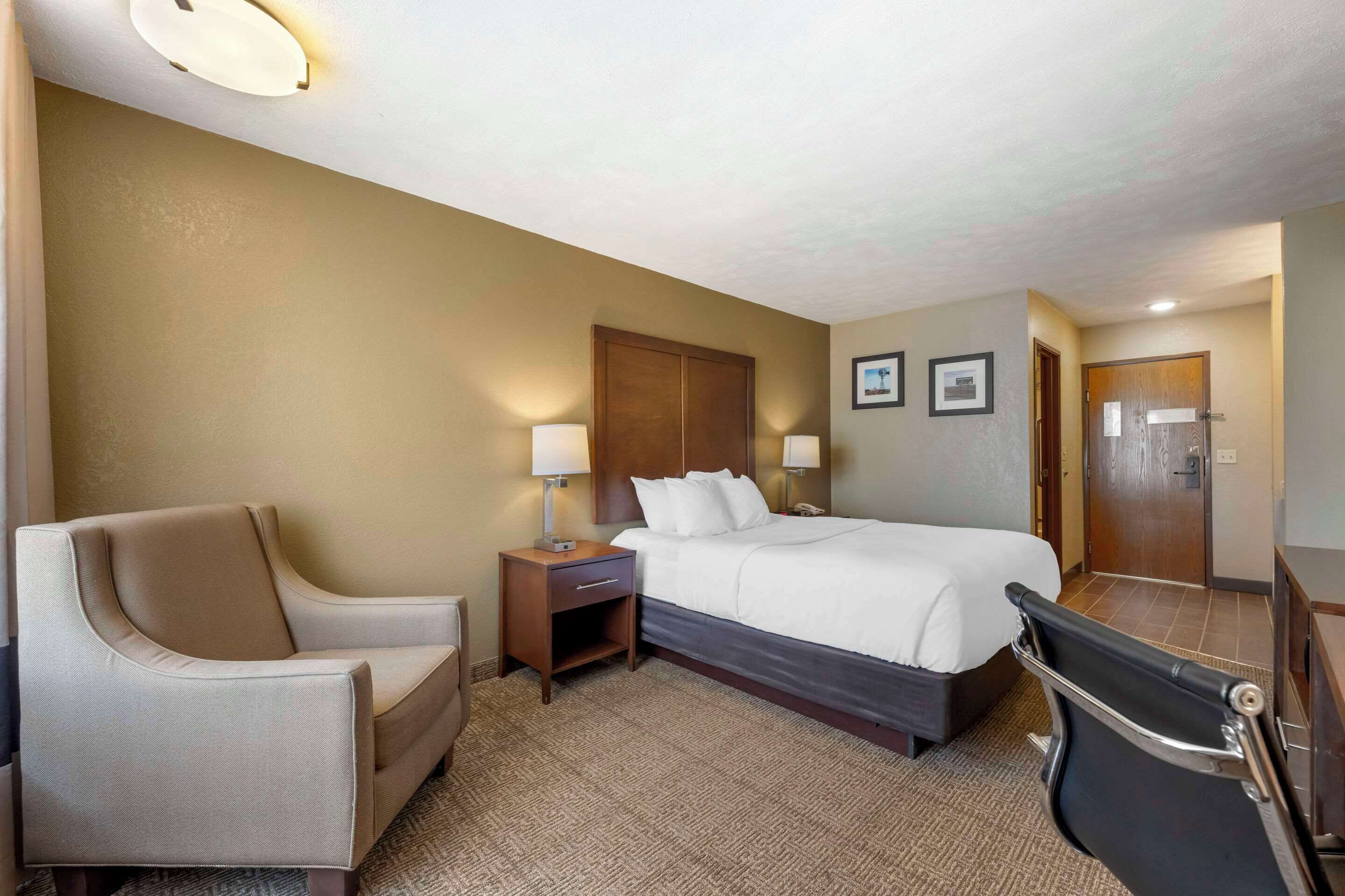 Una habitación de hotel con una cama, una silla, un escritorio con una lámpara y un baño.