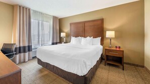 A hotel room with a large bed, two bedside lamps, a wooden nightstand, a desk with a chair, and a window with curtains. - Comfort Inn Lexington (Lexington)